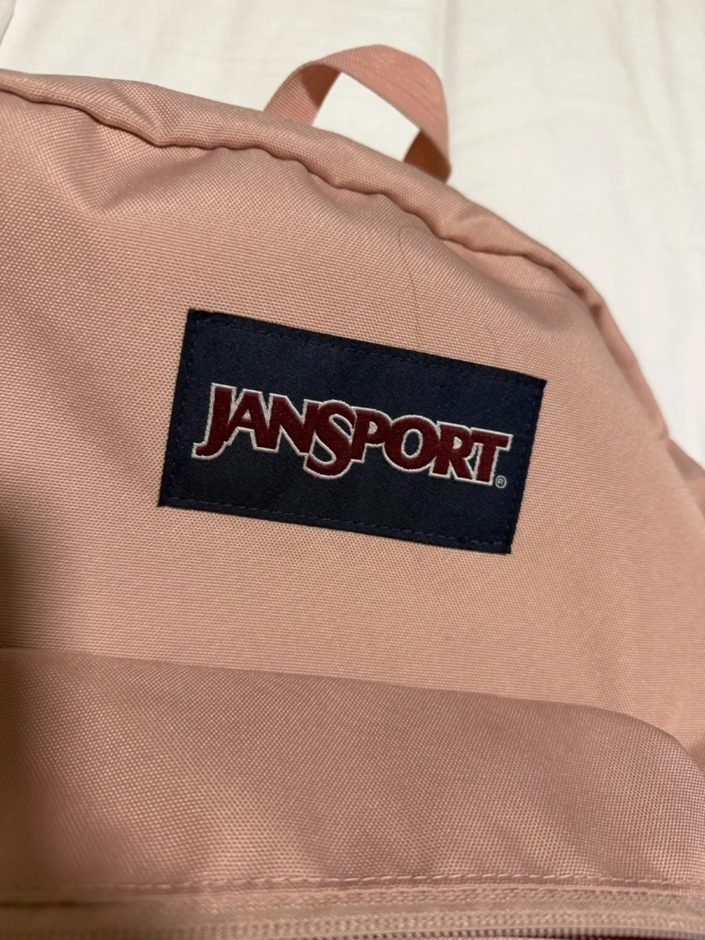 JanSport Cross Town backpack in a light pink color with a blue logo patch